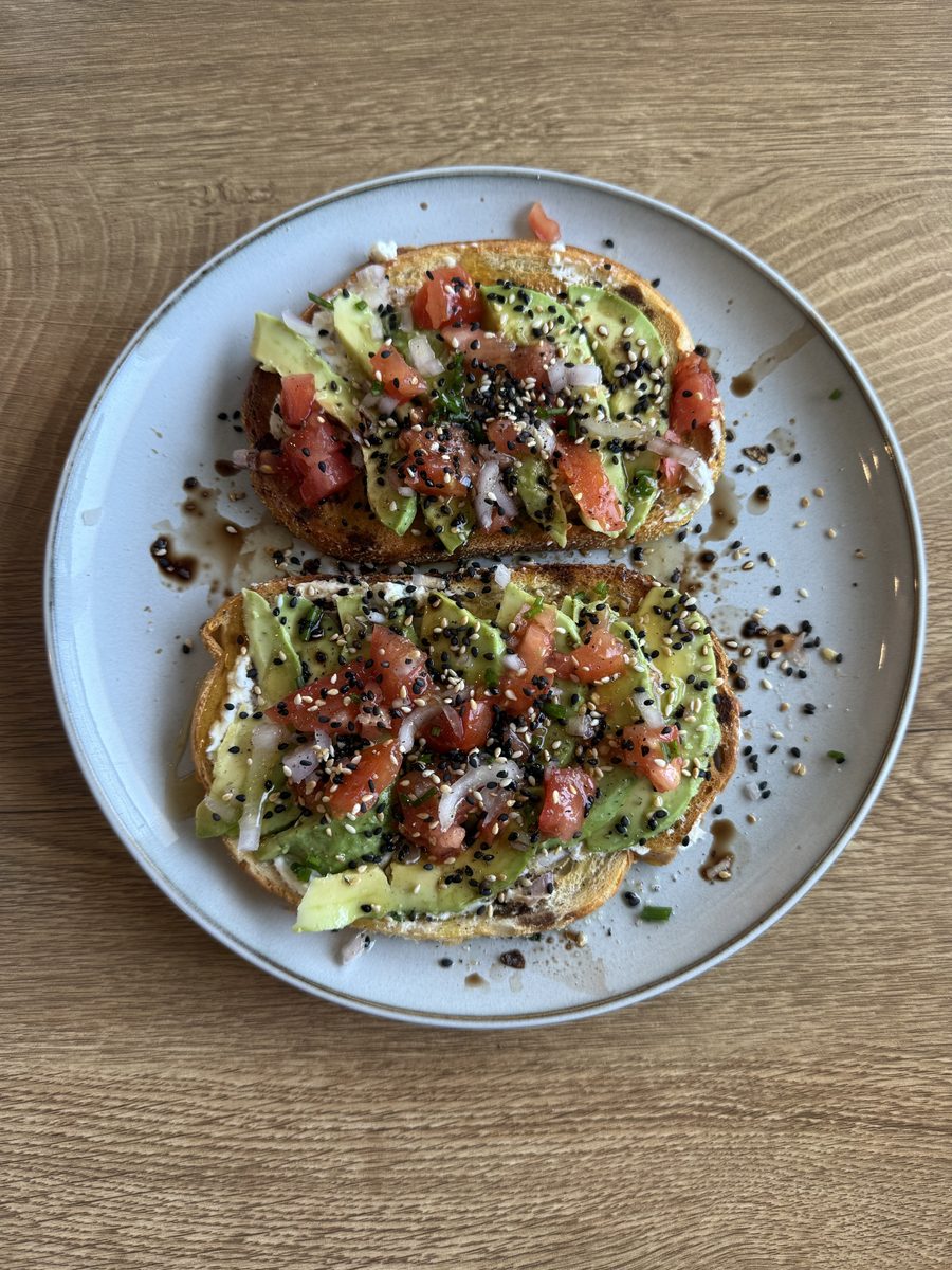 Overhead of two slices of avocado toast topped with diced tomato and everything bagel seasoning on a grey rimmed plate on a wooden