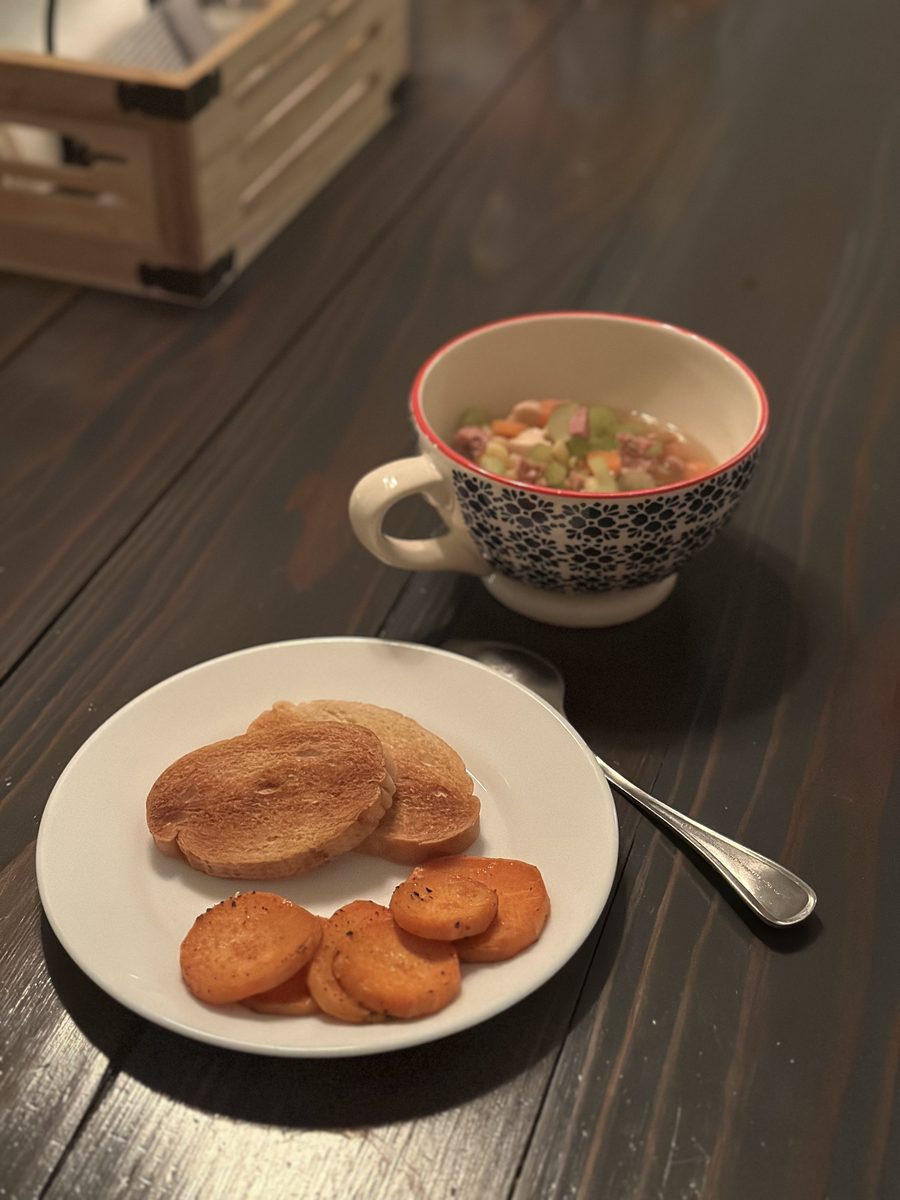 A patterned teacup of chunky bean-and-tomato soup beside a white plate of buttered toast slices and roasted sweet potato rounds on