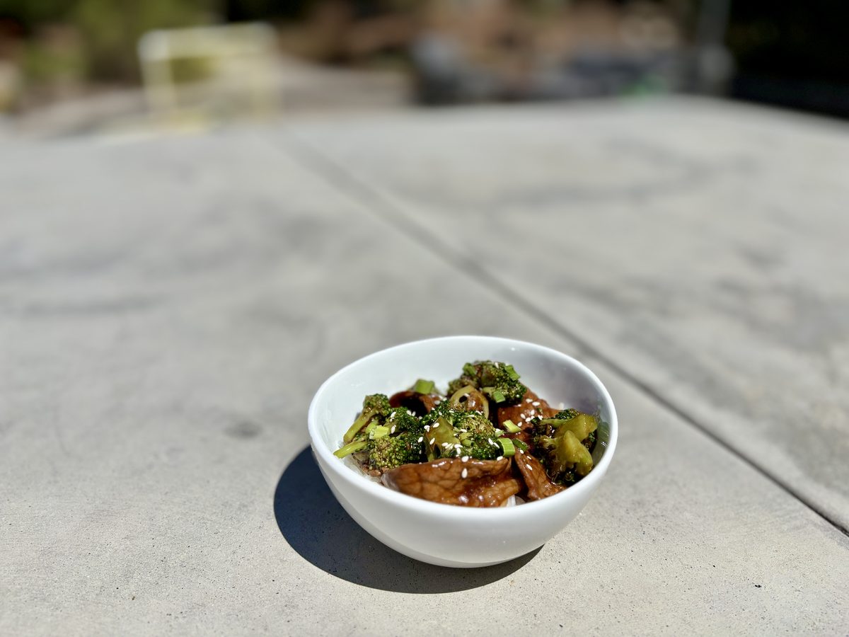 A small white bowl of stir-fry with broccoli florets and dark brown chunks that appear to be braised meat in a glossy sauce, on a