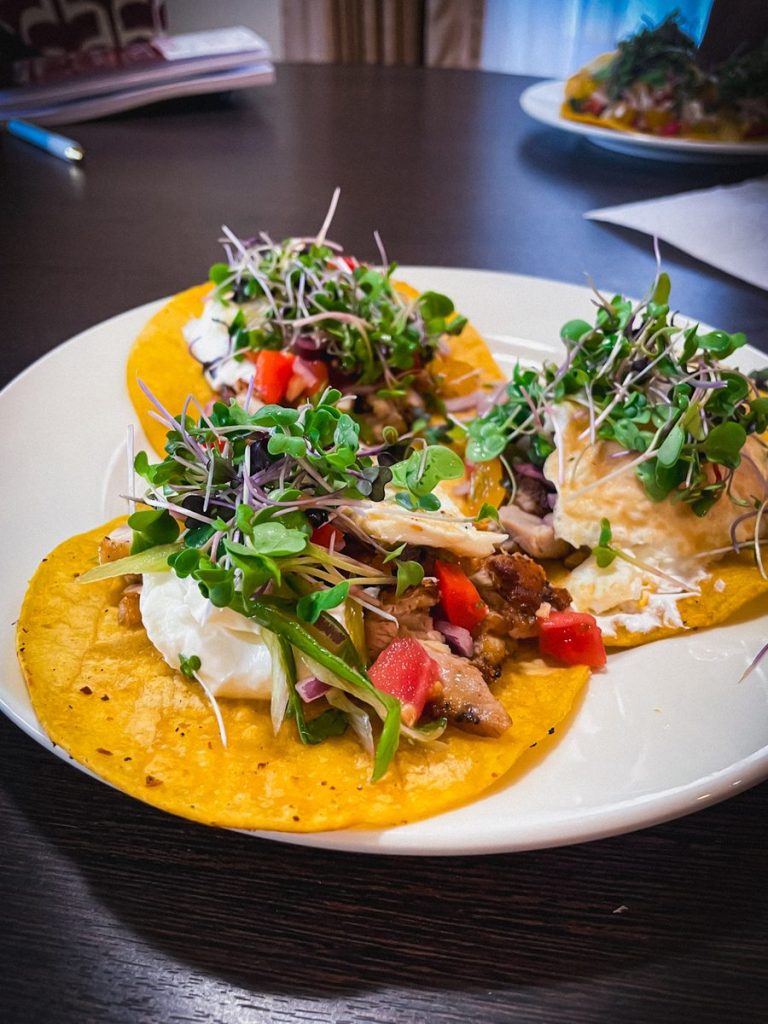 Two breakfast tacos on corn tortillas topped with microgreens and salsa