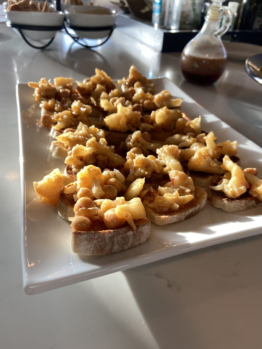 A white rectangular platter of crostini toasts heaped with roasted cauliflower florets and chickpeas, on a white counter with an o