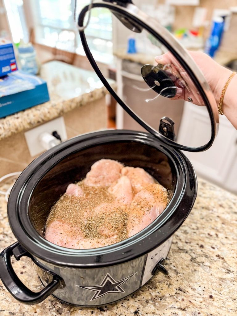 Seasoned raw chicken breasts in an open slow cooker on a kitchen counter