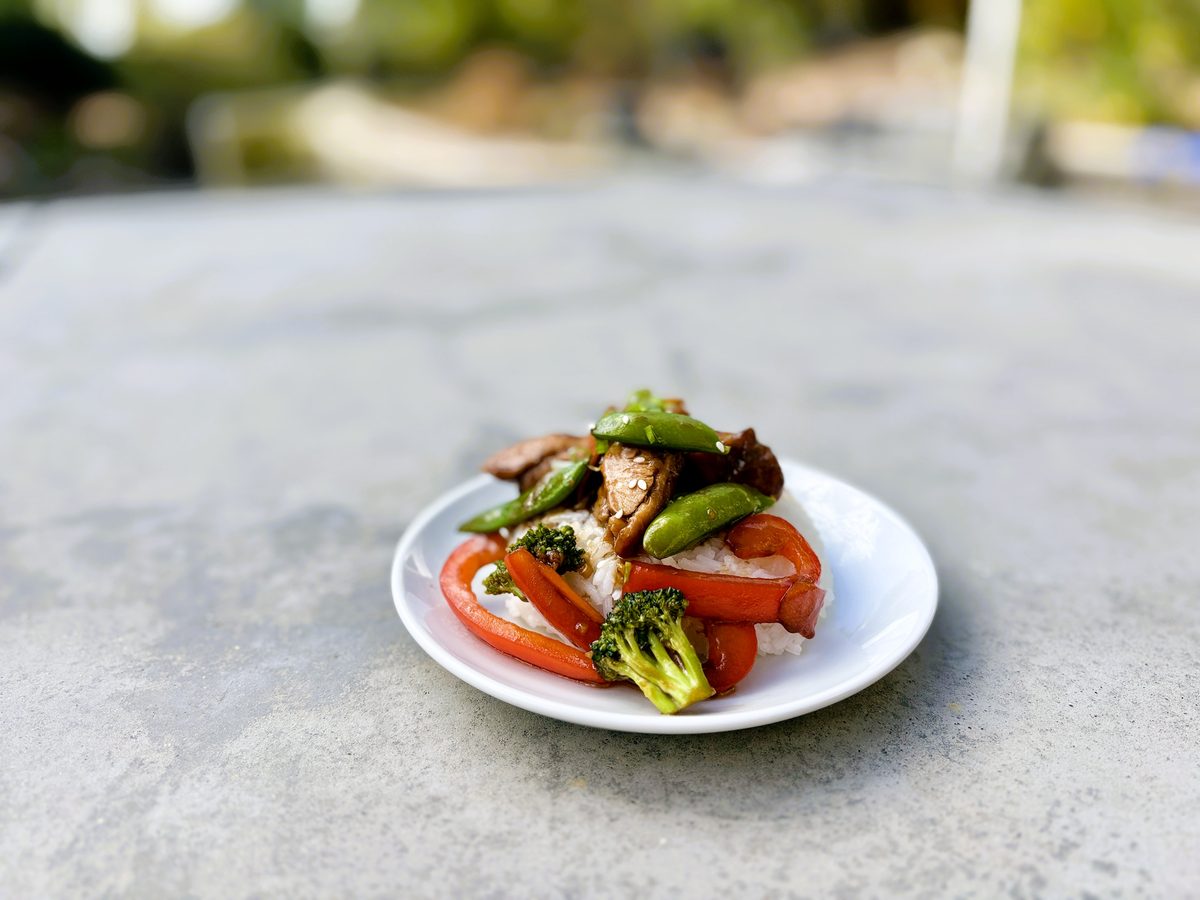 a small white plate with a modest portion of stir-fried chicken, broccoli and red pepper on a stone counter