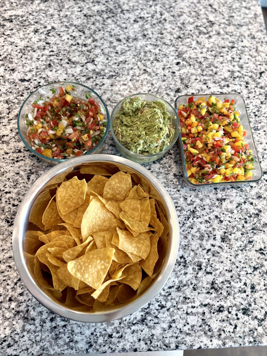 An overhead shot on speckled granite of a metal bowl heaped with tortilla chips beside a glass bowl of pico de gallo, a glass bowl
