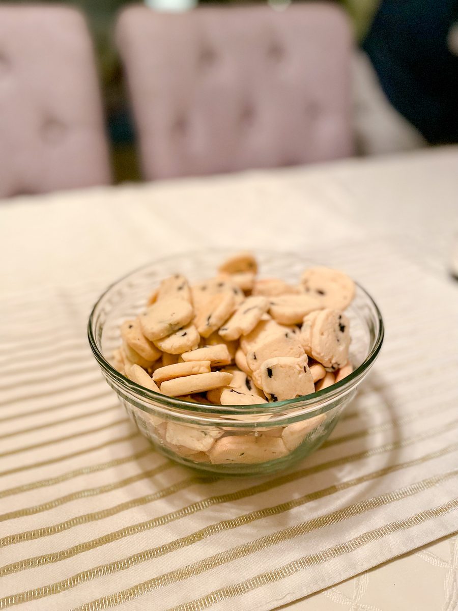 A clear glass bowl piled with small pale shortbread cookie bites flecked with chocolate chips, sitting on a striped table runner o