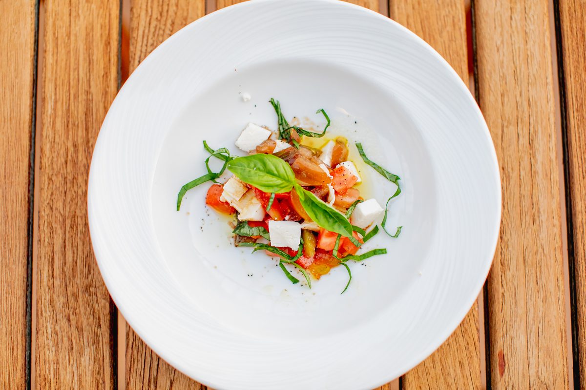 Overhead shot of a chopped caprese salad — diced tomato, cubed fresh mozzarella, basil chiffonade and a whole basil leaf with oliv