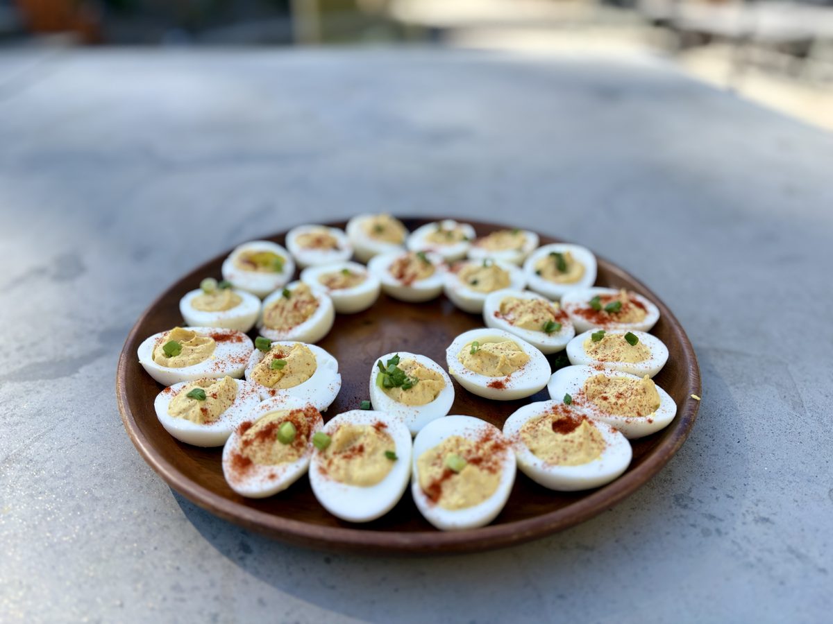 A round terracotta platter on a grey table arranged with a ring of deviled egg halves piped with yellow filling and dusted with pa