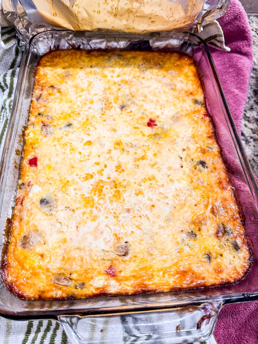 A baked cheesy egg casserole in a glass baking dish resting on striped and pink kitchen towels, golden browned at the edges with f
