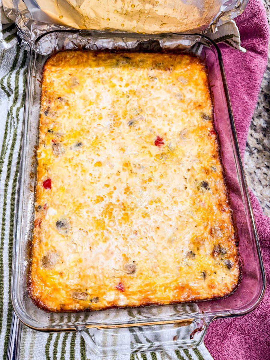 Overhead view of a golden baked egg and cheese casserole in a rectangular glass dish on kitchen towels, red pepper and dark inclus