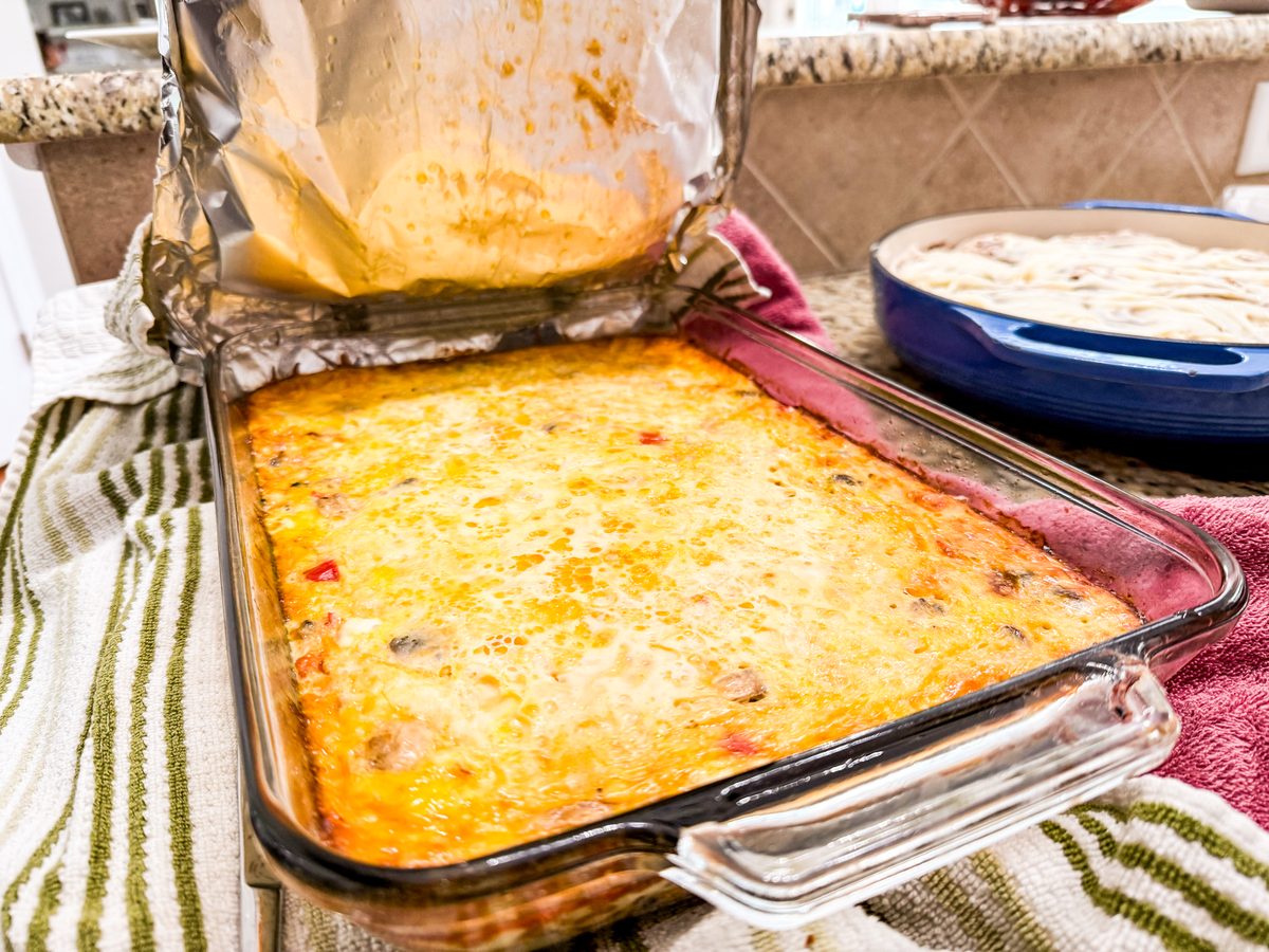 A rectangular glass dish of baked egg casserole with browned cheese on top, sitting on striped kitchen towels on a counter, a seco