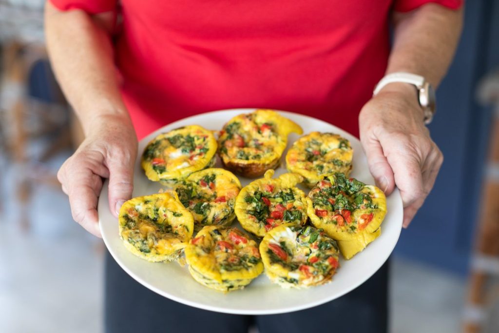 A plate of baked egg muffins with peppers and herbs, held in two hands