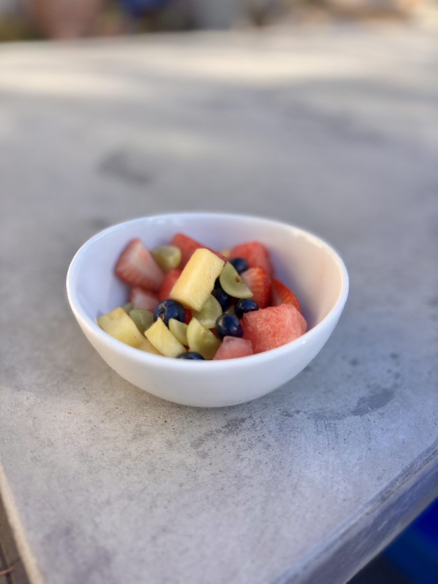 A small white bowl of watermelon, pineapple, grape and blueberry fruit salad sitting on a grey stone counter.