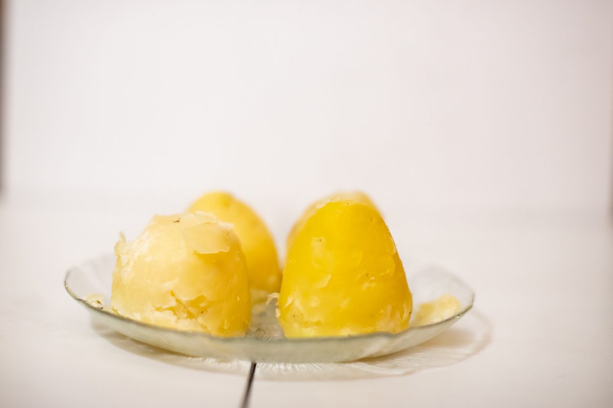 Two pale scoops of mashed potato on a clear glass plate against a plain bright white background, softly lit and low in contrast