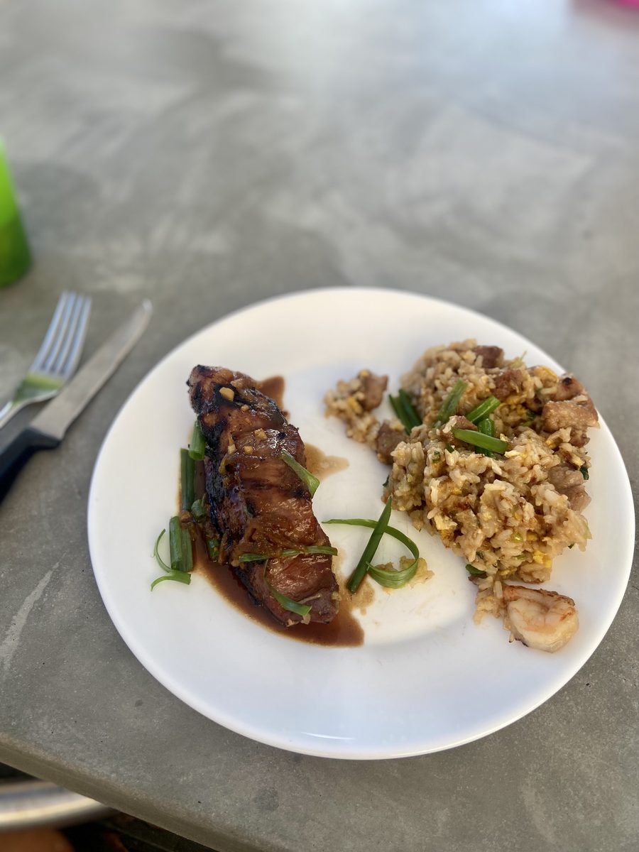 A white plate with a glazed dark-sauced strip of sliced meat topped with scallion next to a portion of fried rice with mushrooms,