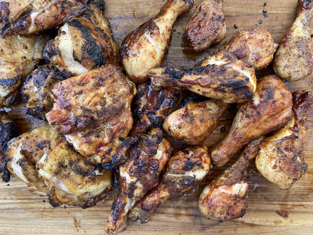 Grilled chicken thighs and drumsticks with charred grill marks spread across a wooden cutting board, filling the frame