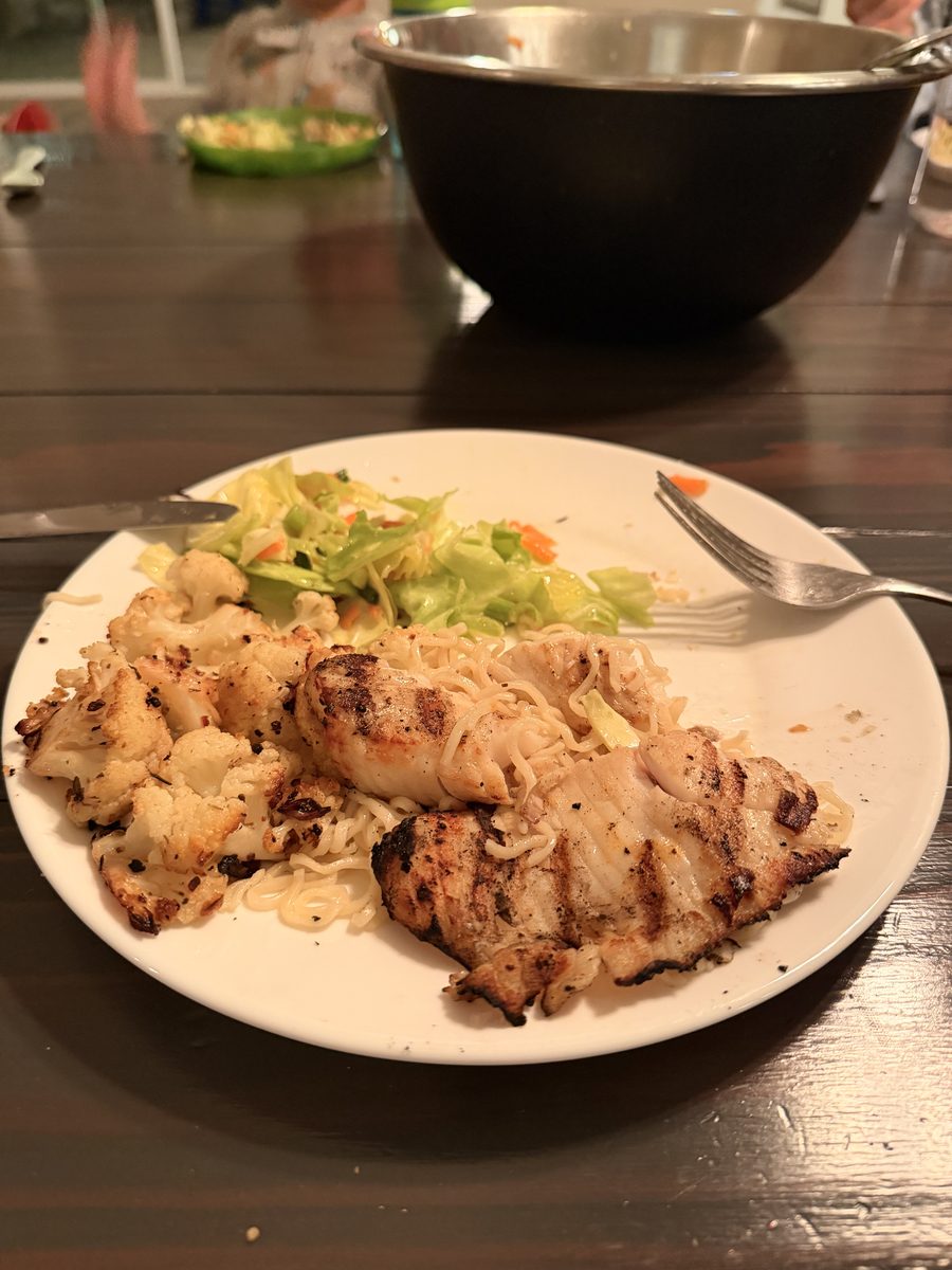Grilled chicken breast with roasted cauliflower and a small pile of shredded cabbage slaw on a cream plate at a dark dining table