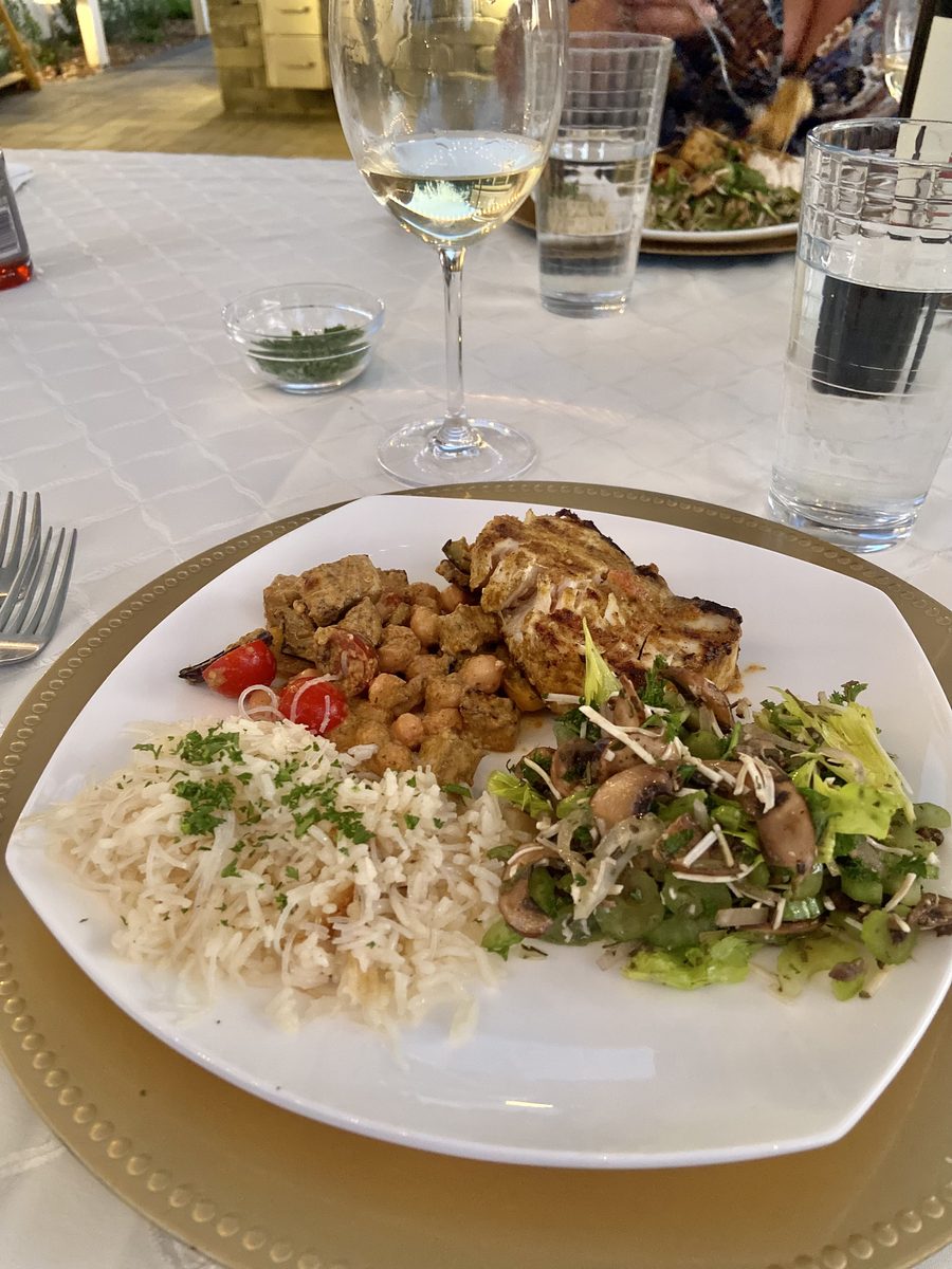 A plated dinner of grilled chicken, chickpea and tomato stew, herbed rice and a mushroom-and-parmesan green salad on a white plate