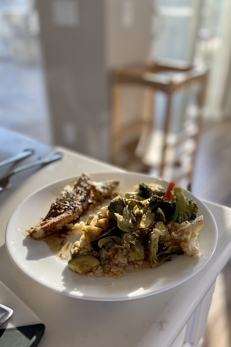 Somewhat blurry: a white plate holding quinoa or grain, dark roasted greens and peppers, and a browned protein portion whose type 