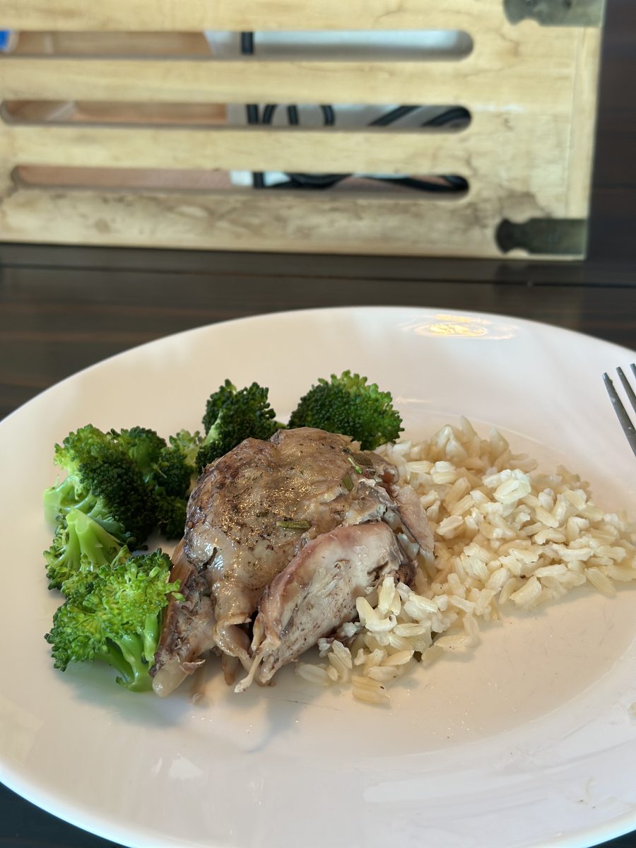 A sliced pork chop with steamed broccoli and brown rice on a large white plate on a dark table, dim indoor lighting with a knife b
