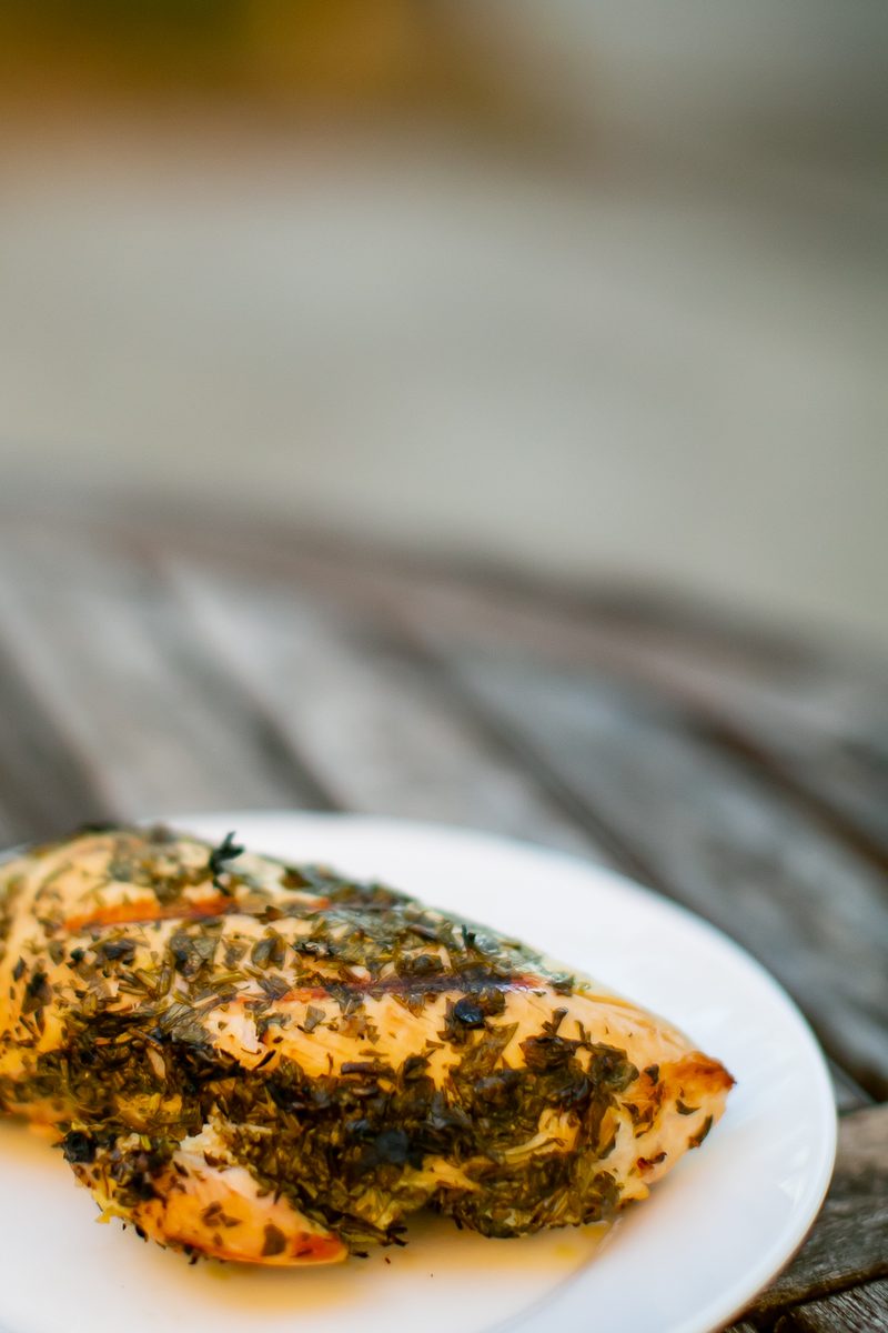 A single herb-crusted chicken breast served on a white plate on a weathered wooden table, shot from a low angle.