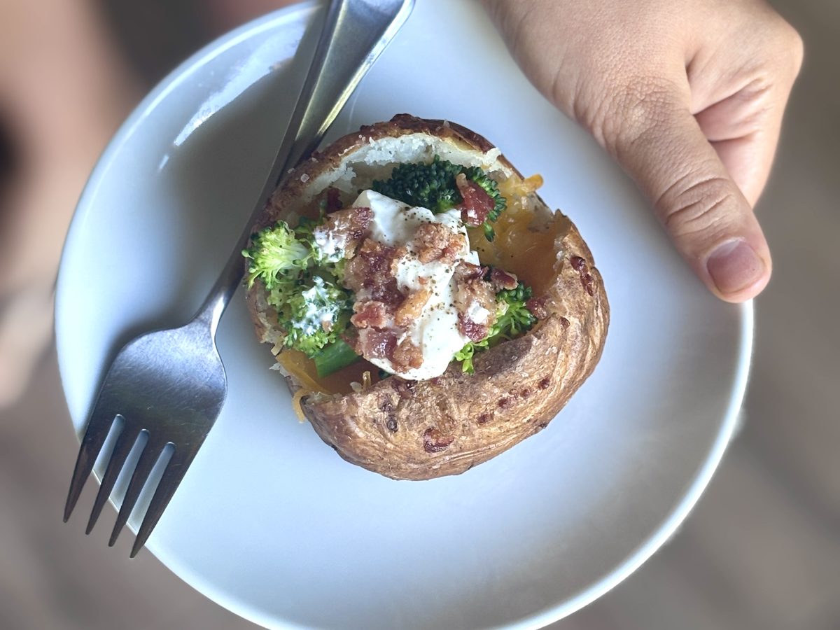 Overhead close view of a hand holding a light blue plate with a loaded baked potato topped with broccoli, melted cheese, sour crea