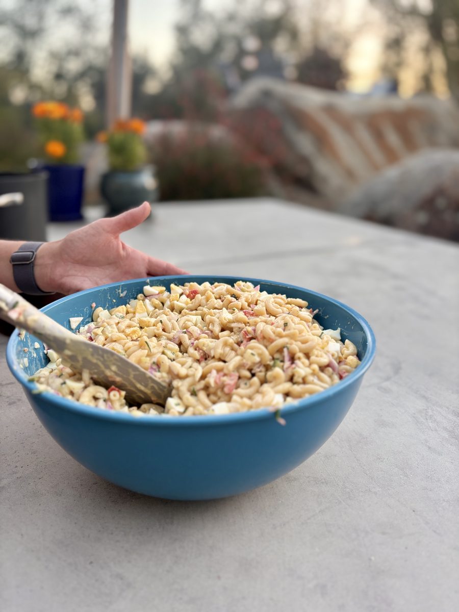 A finished creamy macaroni salad flecked with pink and white bits (possibly diced ham or red pepper, too small to be sure) sitting