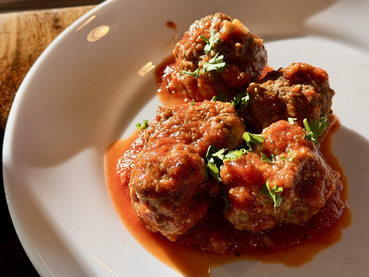 A tight close-up of four meatballs in rich tomato sauce topped with chopped parsley on a white plate.