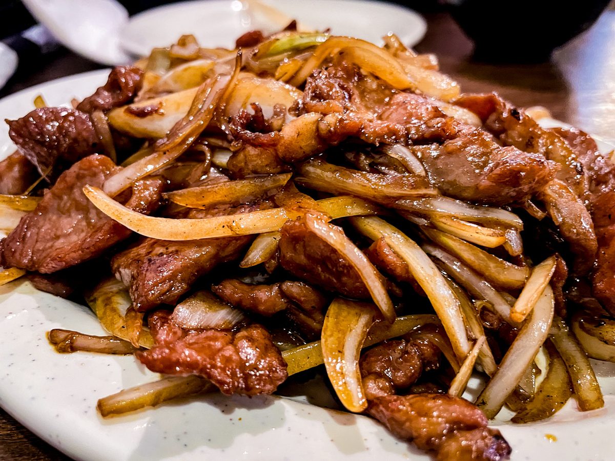 A serving platter heaped with strips of stir-fried beef and sliced onions coated in a dark glossy sauce.