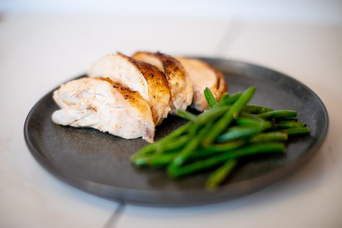 A dark plate with sliced roasted chicken breast fanned beside a pile of green beans.