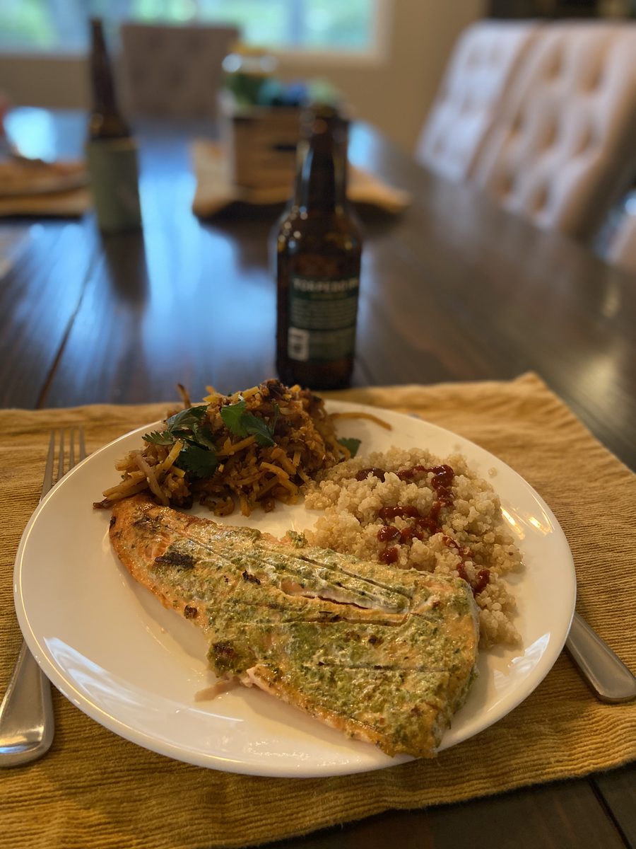 A white dinner plate on a woven placemat with a long herb-and-pesto-crusted salmon fillet, quinoa studded with dried cranberries a