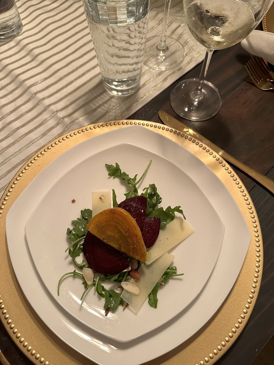 A small composed salad of roasted red and golden beet wedges over arugula with shaved parmesan sheets and goat cheese, on white pl