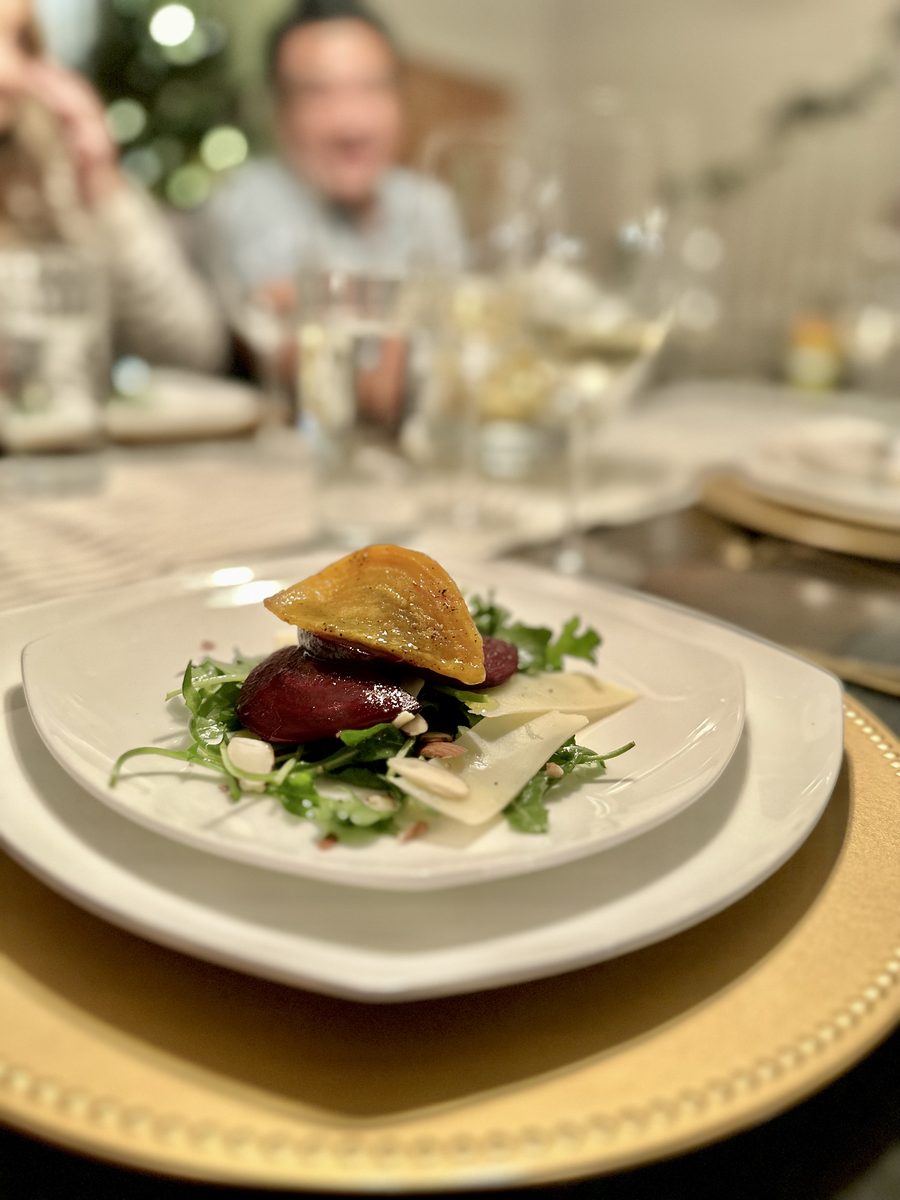 The same plated beet and arugula salad with shaved parmesan and goat cheese on white plates, with a heavily out-of-focus seated ma