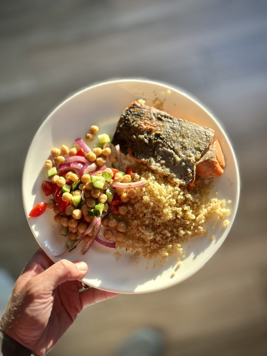 a hand holding a plate of a crusted salmon fillet over quinoa with chickpeas, radish and greens