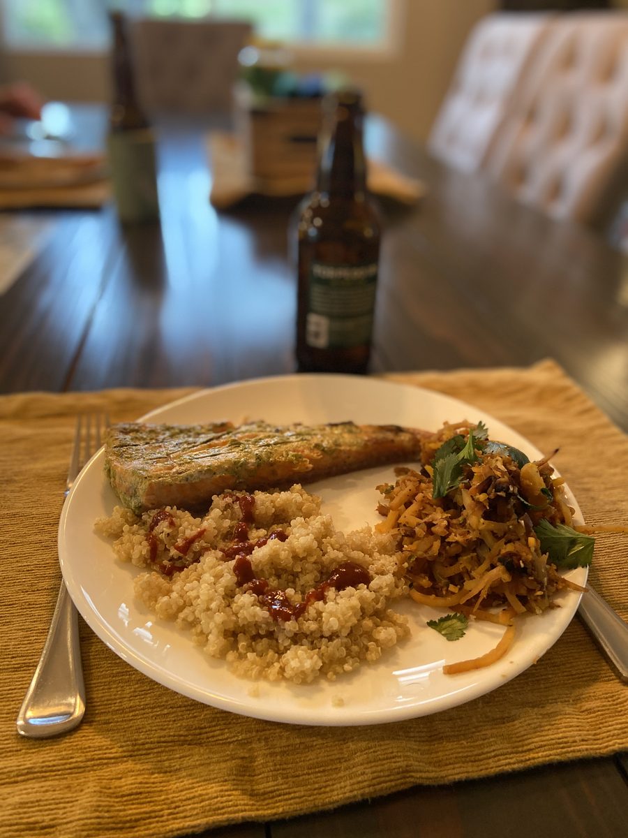 A white plate on a woven placemat with a herb-crusted salmon fillet, quinoa with dried cranberries and a shredded vegetable slaw,
