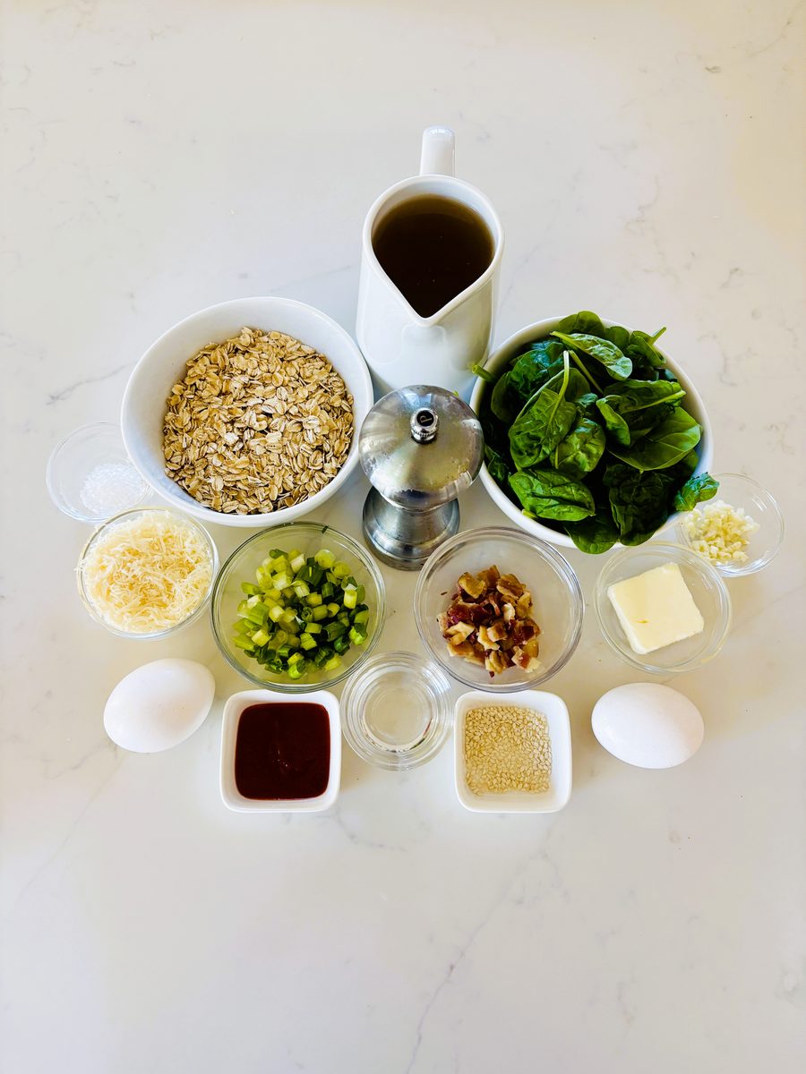 Overhead flat lay of prep bowls on white marble holding rolled oats, baby spinach, peas, walnuts, butter, grated parmesan, an egg,