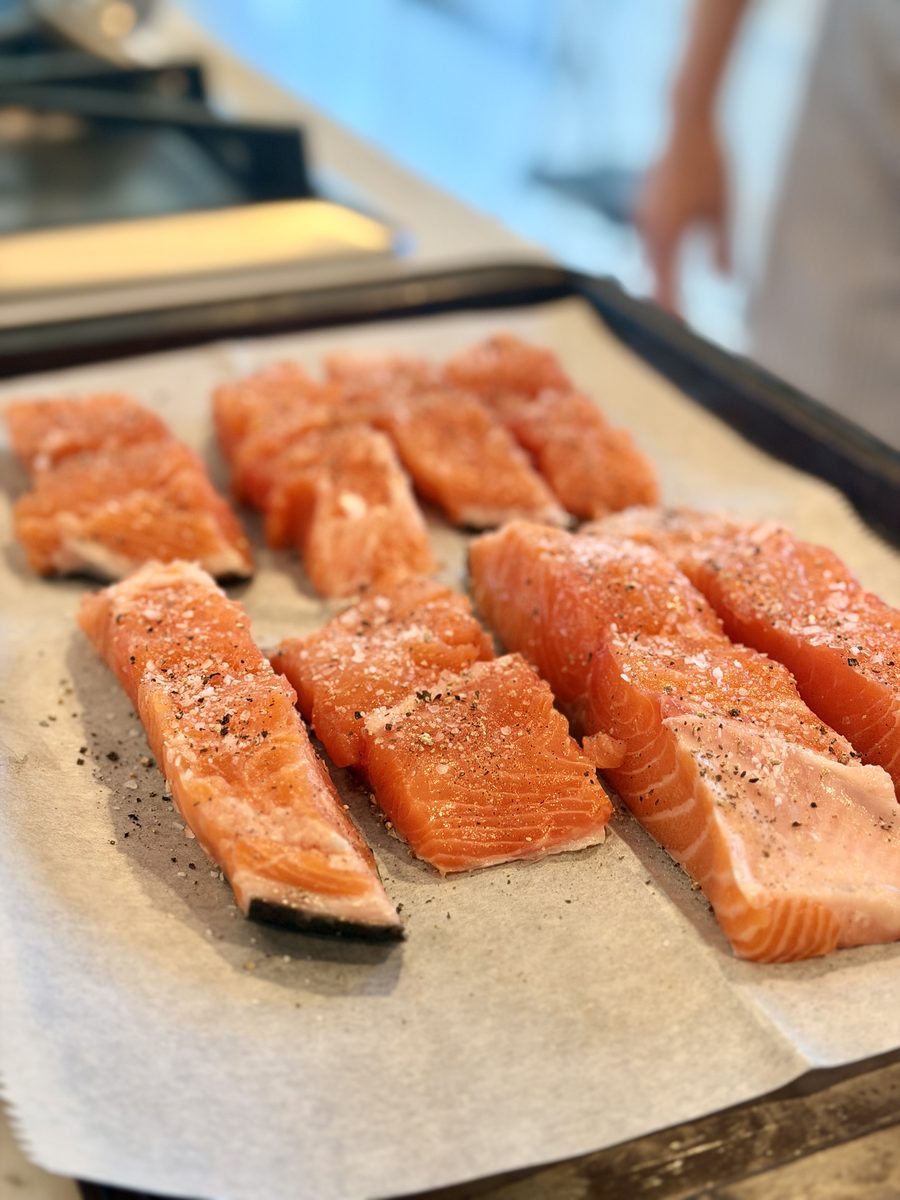 Overhead close-up of six raw seasoned salmon fillets arranged on parchment paper on a sheet pan.