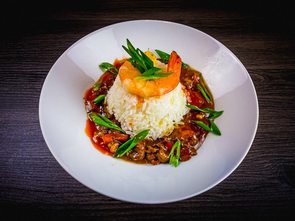 A molded round of white rice topped with shrimp and green beans, ringed by chunky red creole sauce on a white plate over dark wood