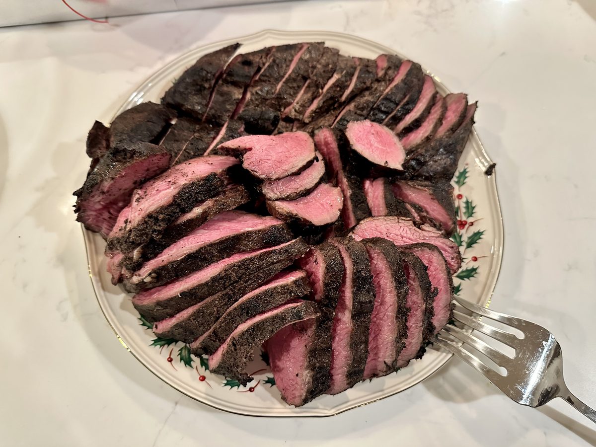 Overhead close-up of a fanned platter of sliced beef tenderloin with rosy pink centers and dark crust, a serving fork at the right