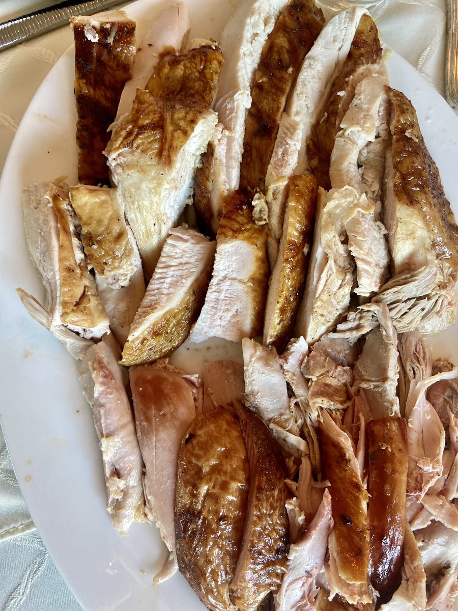 Tight overhead crop of sliced roasted turkey breast and dark meat piled on a white platter under harsh light.