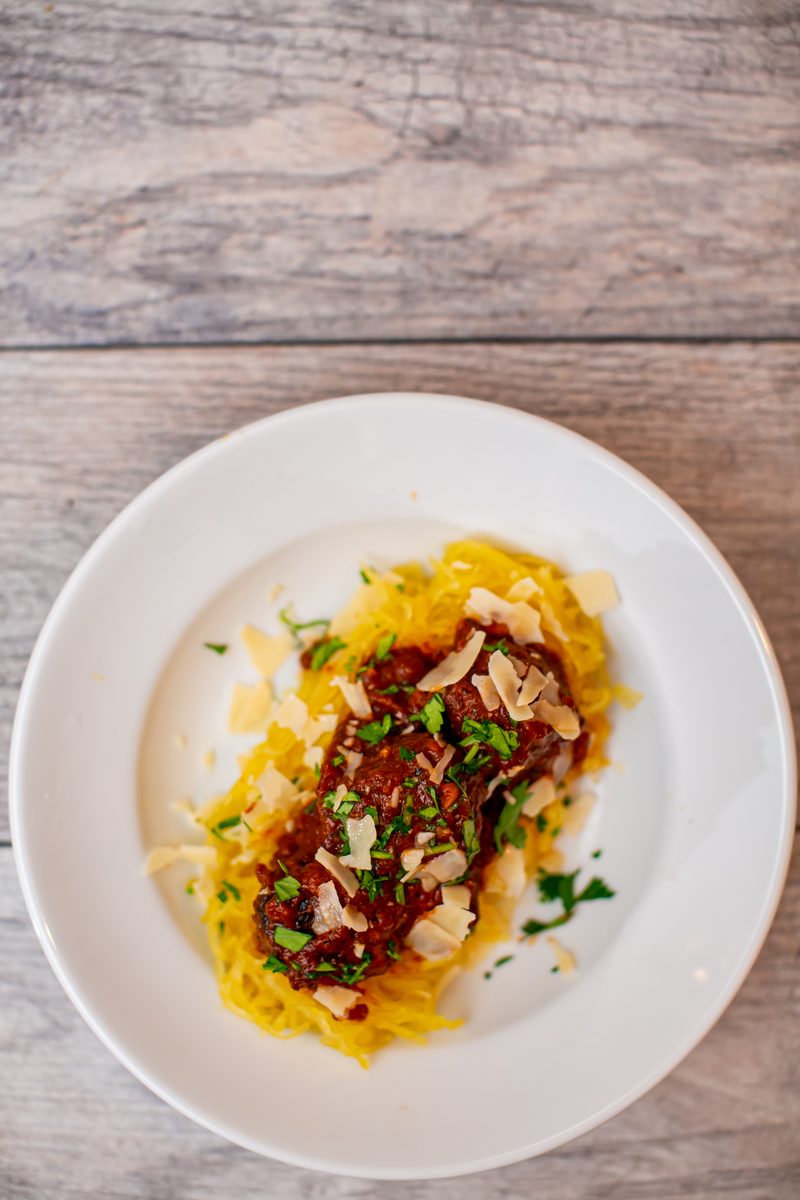 Overhead shot of a white plate of roasted spaghetti squash strands topped with a chunky dark red sauce, shaved parmesan and parsle