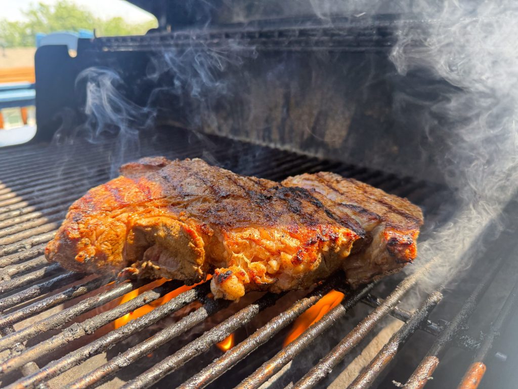 A seasoned steak searing over open flames on a gas grill, smoke rising around the grates
