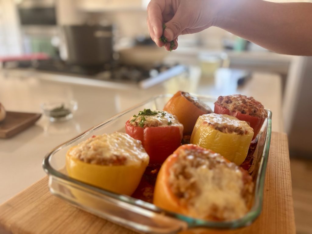 Baked stuffed peppers in a glass dish, being garnished by hand