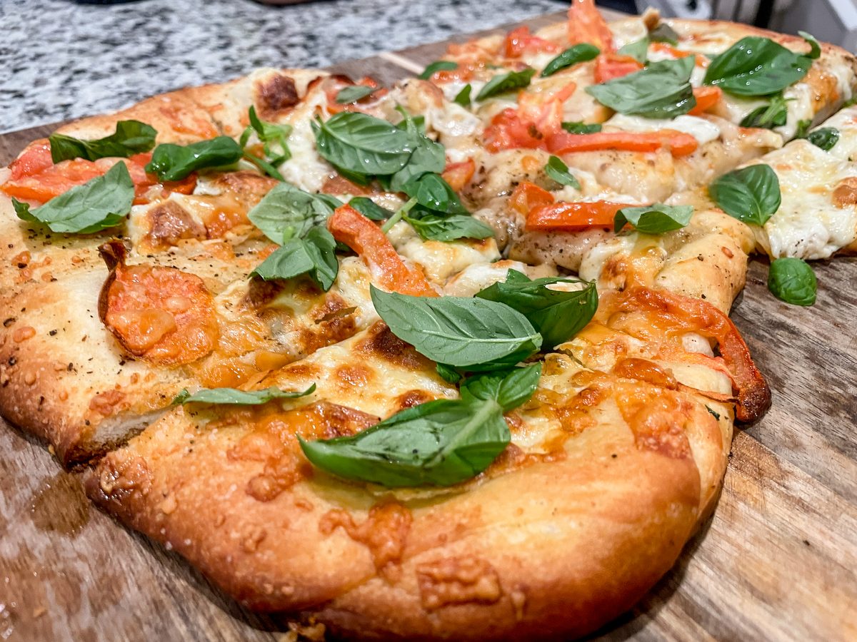Baked flatbread pizza with melted mozzarella, tomato slices and whole basil leaves on a rustic wooden table, shot close from the s
