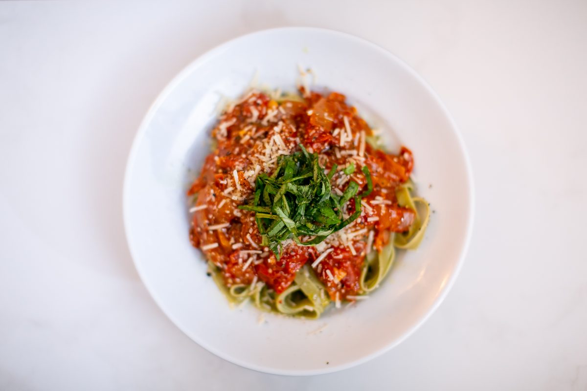 Overhead white plate of pasta ribbons in chunky tomato sauce topped with grated parmesan and torn basil.