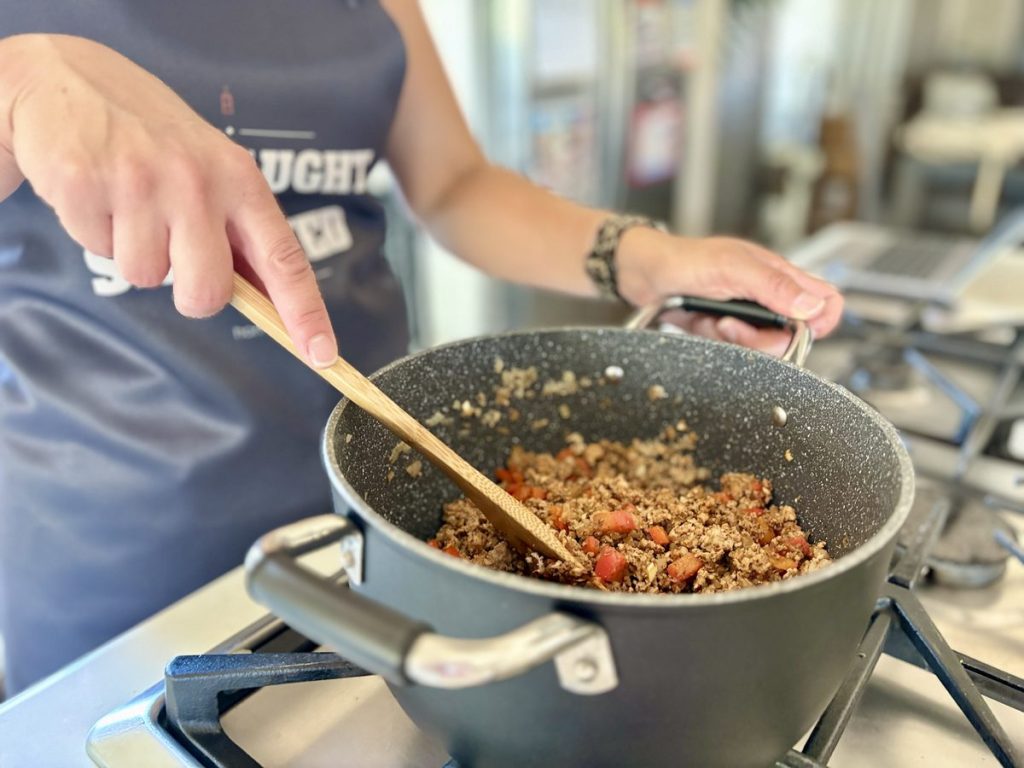 Turkey chili cooking in a pot on the stove, being stirred with a wooden spoon