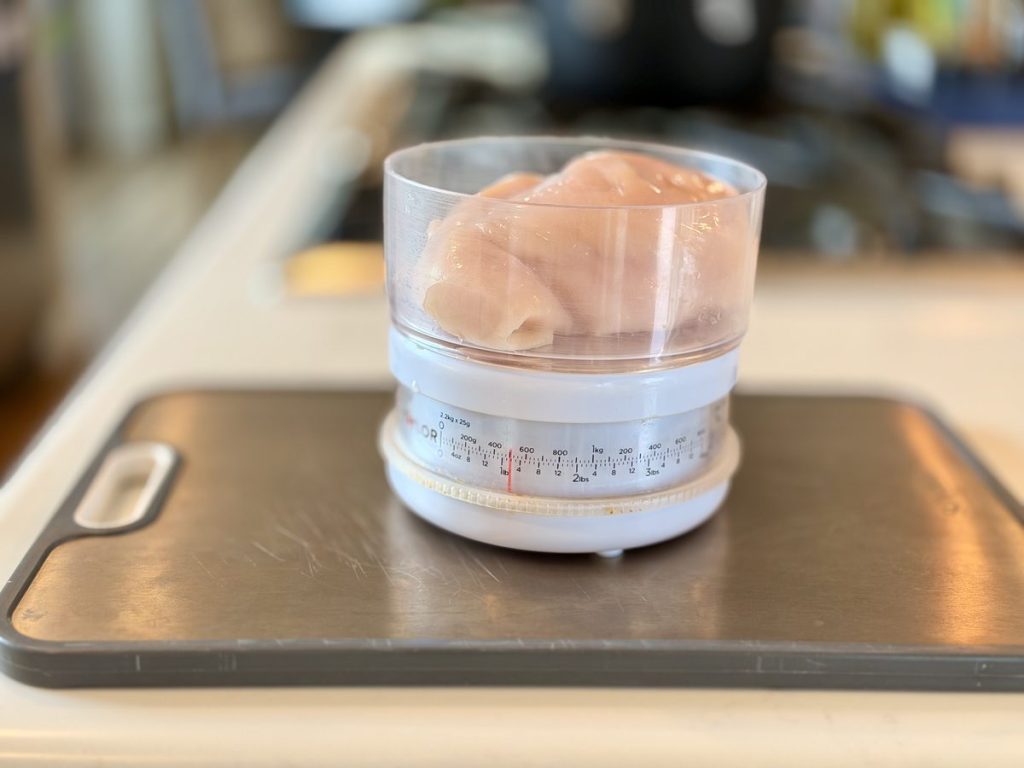 Raw chicken breast being weighed on a digital kitchen scale