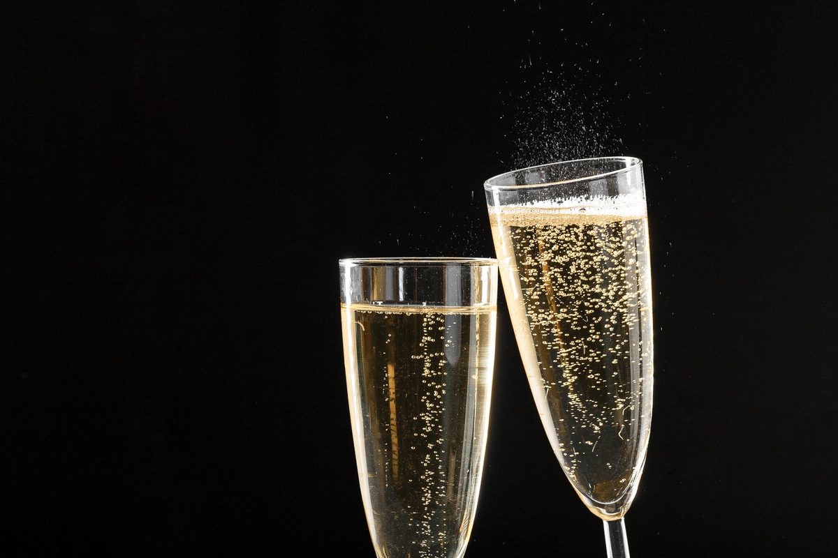 Two champagne flutes filled with sparkling wine, backlit against a dark background with golden bokeh