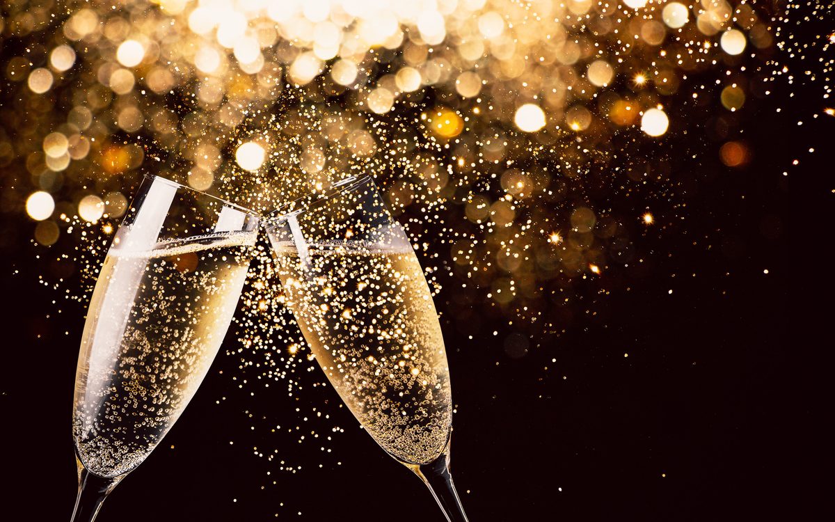 Two champagne flutes clinking in a toast, sparkling wine catching the light against a dark background