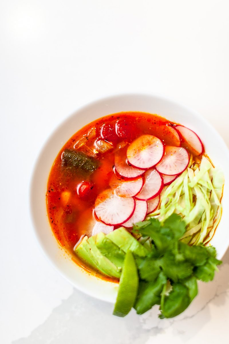 Overhead view of a white bowl of cold noodles in a bright red broth topped with sliced radishes, shredded cabbage, a strip of seaw