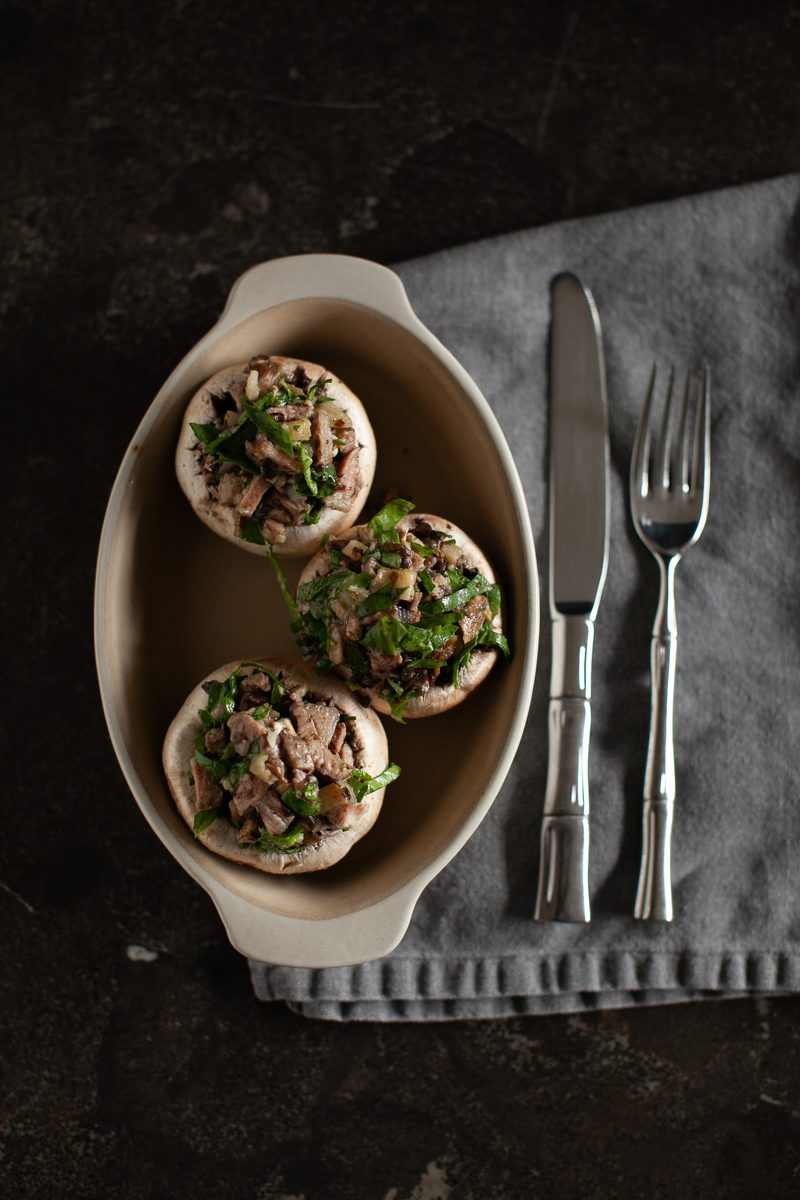 Overhead shot of three large white mushroom caps stuffed with a chopped mushroom, herb and nut filling in a small oval ceramic dis